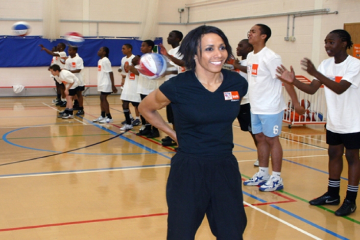Dame Kelly_Holmes_in_front_of_boys_playing_basketball