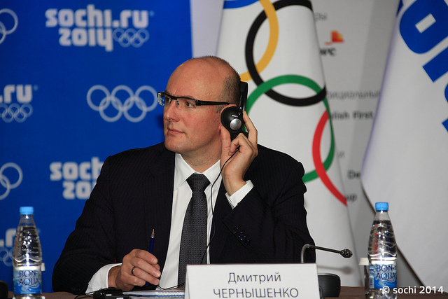 Dmitry Chernyshenko_with_ear_piece_in_front_of_Sochi_2014_logo