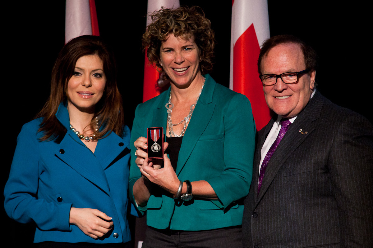 Marnie McBean centre receives the Queen Elizabeth II Diamond Jubilee Medal from Marcel Aubut right and Parliamentary assistant to the Minister of Veteran Affairs Eve Adams left