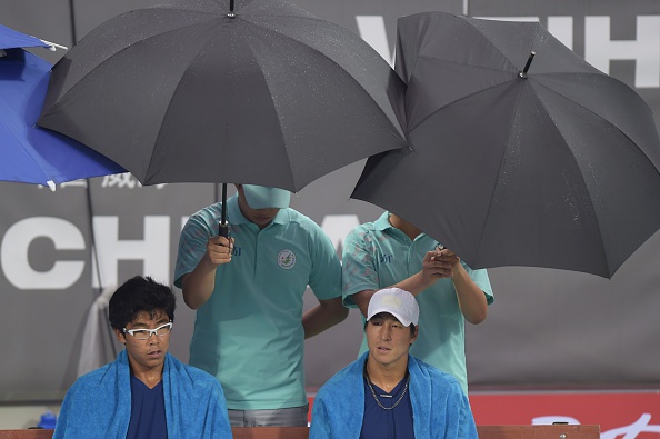 South Korea's Lim Yongkyu and Chung Hyeon sit under umbrellas as rain falls during their mens doubles final tennis match against India's Saketh Sai Myneni and Sanam Krishan Singh ©Getty Images