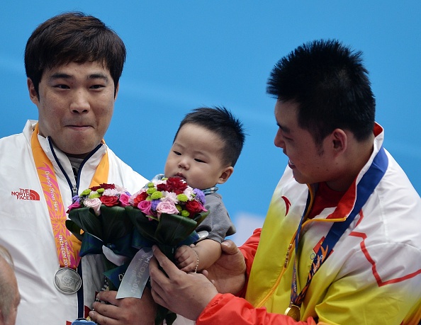 China's Yang Zhe plays with the eight-month old son of South Korea's Kim Min-jae on the weightlifting podium ©AFP/Getty Images