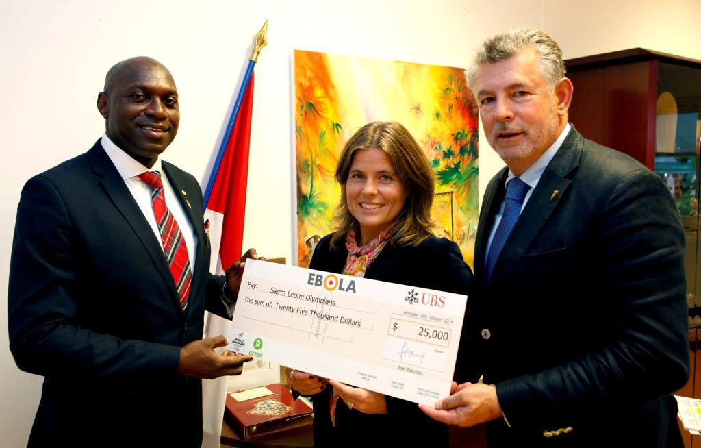 Joël Bouzou (right), WOA President, and Pernilla Wiberg (centre), two-time Olympic gold medallist, present Dr Francis Dove Edwin (left) with funding for the first #TargetEbola container of supplies ©WOA